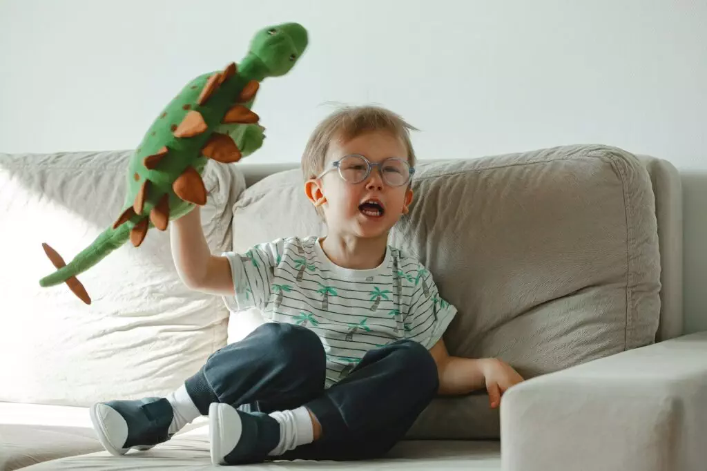 Un enfant autiste à lunettes est assis sur le canapé est triste et en colère